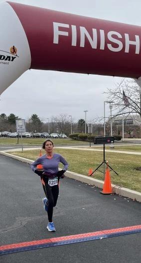 Runner crossing the finish line with the Run The Day bib-number keypad open on a phone